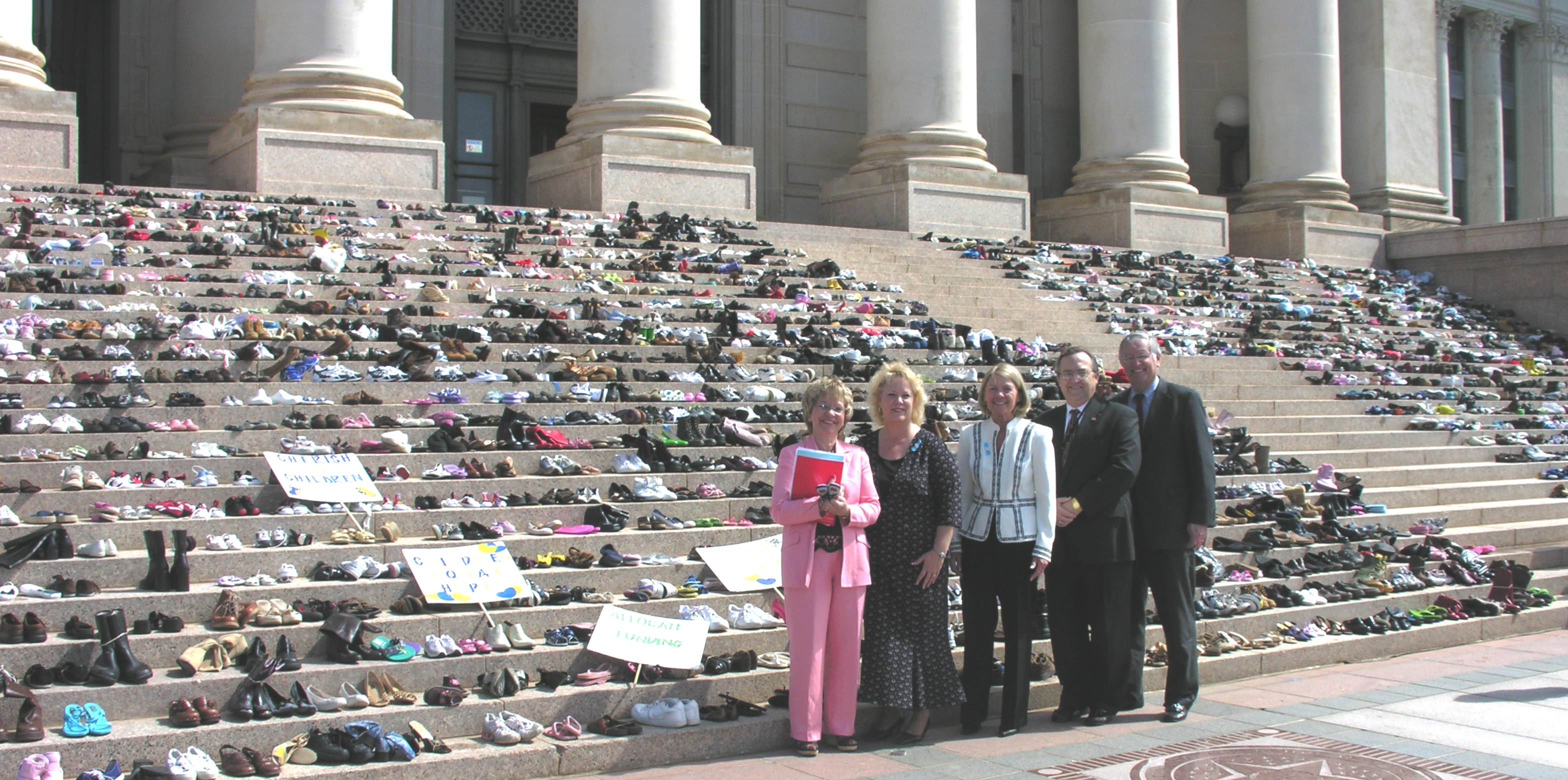 Legislators and officials pose with shoes on Capitol steps.